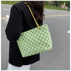 Outdoor street view of green checkerboard tote bag with embossed texture and chain strap