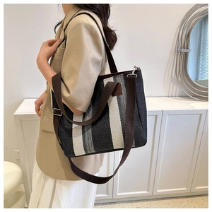 Close-up of a striped woven canvas tote bag with adjustable straps on a model in a minimal room