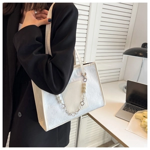 Detail of white tote bag with floral texture, pearl chain and clover charm decoration