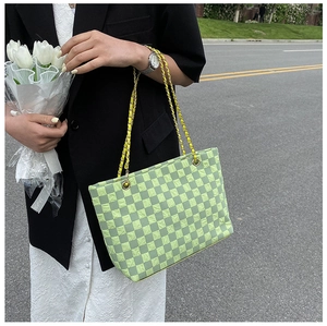 Close-up of a light green checkerboard tote bag with a golden chain strap on a model