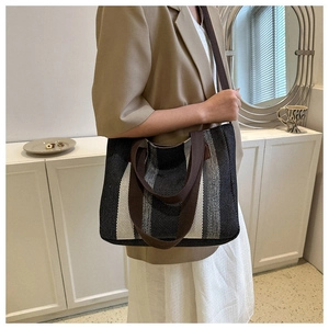 Detail of a large striped tote bag featuring woven texture and brown webbing handles