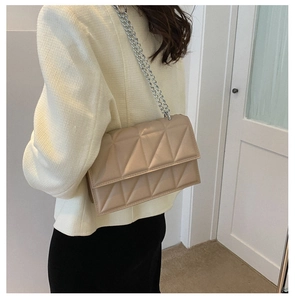 Detail of a beige quilted crossbody bag with silver chain strap on a model's shoulder