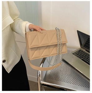 Detail of beige quilted chain shoulder bag with geometric stitching held by a model
