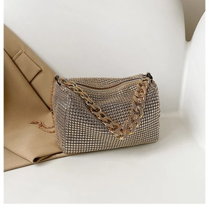 Détail d'un sac à main doré avec strass et anse en chaîne épaisse sur socle blanc