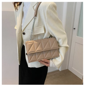 Detail of beige quilted flap crossbody bag with silver metal chain and leather strap