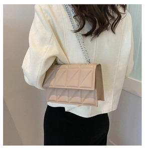 Detail of light brown quilted chain bag worn by model against a white wall
