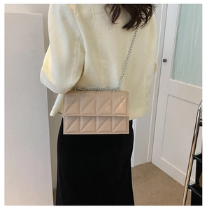 Detail of beige quilted crossbody bag with silver chain strap worn by a model