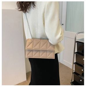Detail of beige quilted crossbody bag with silver chain strap and geometric stitching
