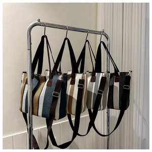 Vertical display of striped canvas tote bags with leather-like handles on a metal rack