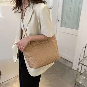 Beige quilted tote bag with gold chain strap worn cross-body for stylish daily commuting