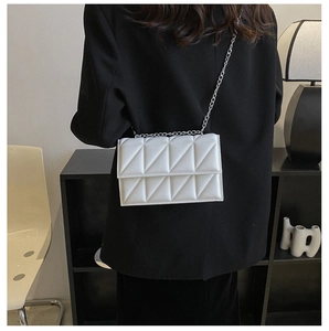 Close-up of white quilted crossbody bag with silver chain strap and geometric stitching
