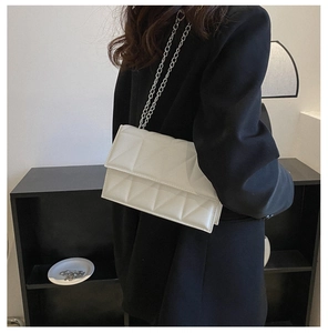 Detail of white quilted crossbody bag with silver chain strap shown on a model