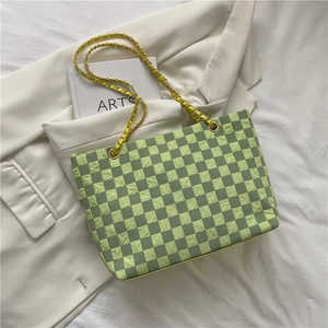 Green checkerboard tote bag with gold chain strap placed on a white suit and artsy book