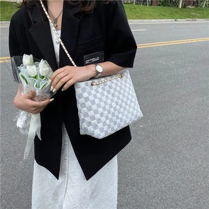 Grey and white checkerboard tote bag with chain strap styled in an outdoor scene