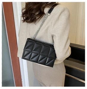 Detail of black quilted crossbody bag with silver chain strap shown on model shoulder