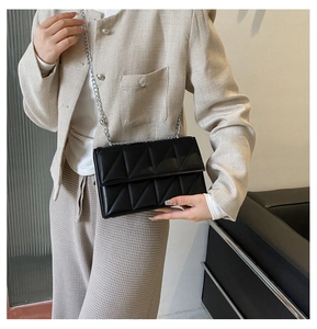 Detail of a black quilted crossbody bag with silver chain strap worn by a model