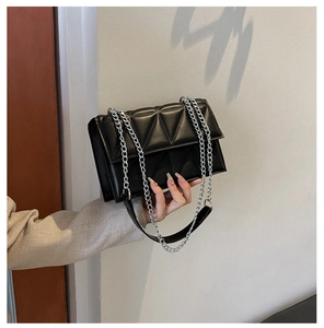 Detail view of black quilted crossbody bag with geometric triangle stitching and silver chain