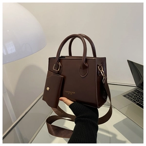 Modern dark brown crossbody bag with mini pouch on a desk with a laptop and lamp