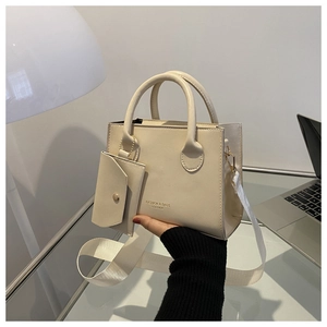 Detail of a beige leather handbag with a mini pouch charm and a wide woven shoulder strap