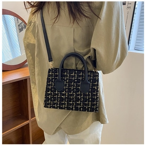 Close-up of black and gold tweed woven handbag with leather handles and gold-tone hardware