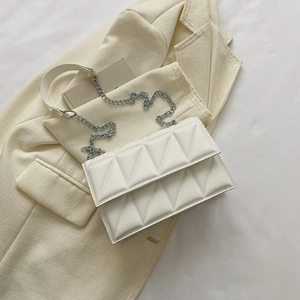 White quilted crossbody bag with silver chain strap on beige blazer background