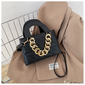Black quilted crossbody bag with chunky gold chain on a tan blazer background