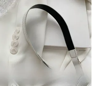 Dettaglio della tracolla bianca con motivo a coccodrillo, fibbia dorata e perle decorative