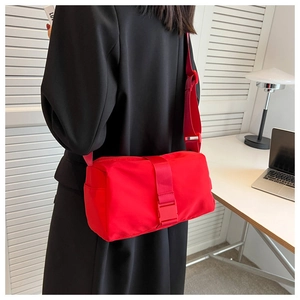 Detail of red oxford nylon crossbody bag with adjustable strap and buckle on black coat