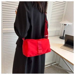 Red nylon crossbody bag with wide shoulder strap worn by model in an office setting