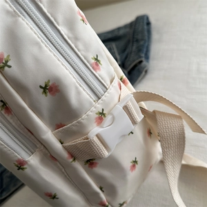 Detail of floral nylon backpack featuring white buckle, zipper and woven shoulder straps