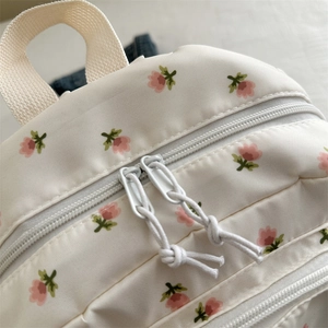 Close-up of white canvas backpack with floral print and dual white metal zippers