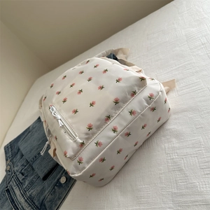 Detailed close-up of a white floral embroidery small backpack on a soft textile surface
