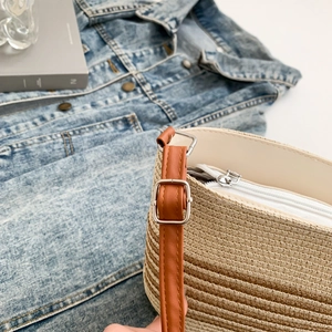 Detail of woven straw texture and brown leather strap with silver buckle on striped bag