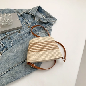 Detail of woven texture with brown stripes and adjustable strap on straw shoulder bag