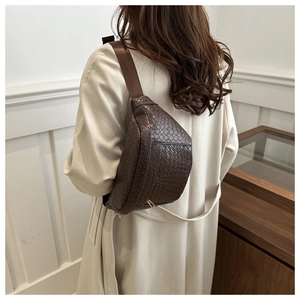 Detail of dark brown croc-embossed chest bag with gold zipper and wide strap on model
