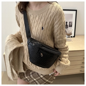 Detail of black woven texture crossbody bag with gold zipper on wide nylon strap