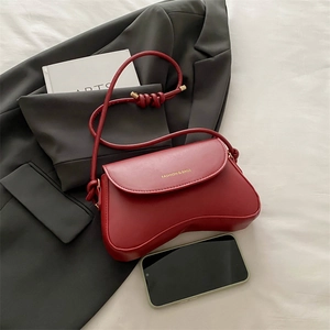 Stylish red leather underarm bag with unique curved base and gold logo on grey background