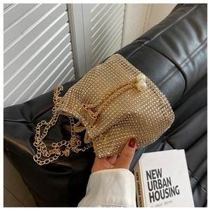 Detailweergave van gouden bucketbag met strass-steentjes, parelkoord en metalen ketting