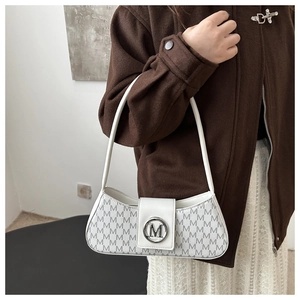 Gros plan du sac sous le bras en cuir blanc cassé avec imprimé monogramme M et logo en métal