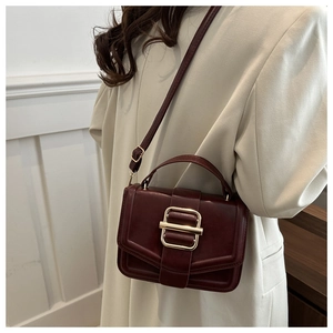 Gros plan d'un sac à bandoulière bordeaux en cuir avec boucle en métal sur une veste