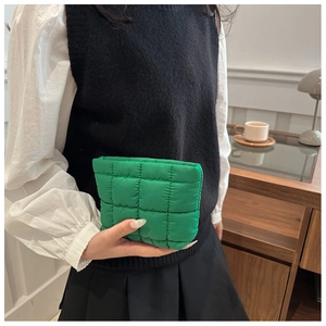 Close-up of bright green quilted makeup pouch held by model in home setting