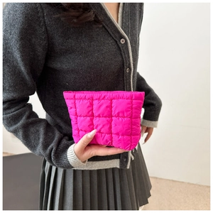 Close-up of vibrant pink quilted puffer pouch held by a model in gray knitwear