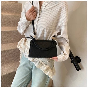 Detail of black embossed square handbag with knotted handle and gold hardware on model