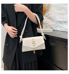 Detail of cream leather shoulder bag featuring a gold S logo and elegant tassel charm