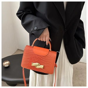 Close-up of orange crocodile pattern texture with golden wave metal clasp and handle