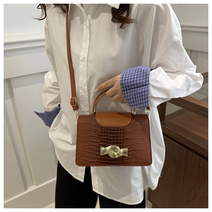 Close-up of caramel brown crocodile embossed leather handbag with golden wave buckle