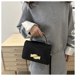 Detail of black crocodile texture bag with gold wavy clasp and metal top handle