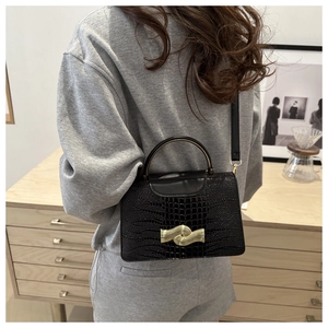 Close-up of black crocodile pattern handbag with stylish wavy golden metal lock and strap