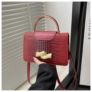 Detail of red crocodile texture handbag with golden metal handle and wave-shaped clasp