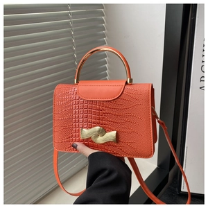 Detail of orange crocodile texture bag with golden metal handle and twist lock closure